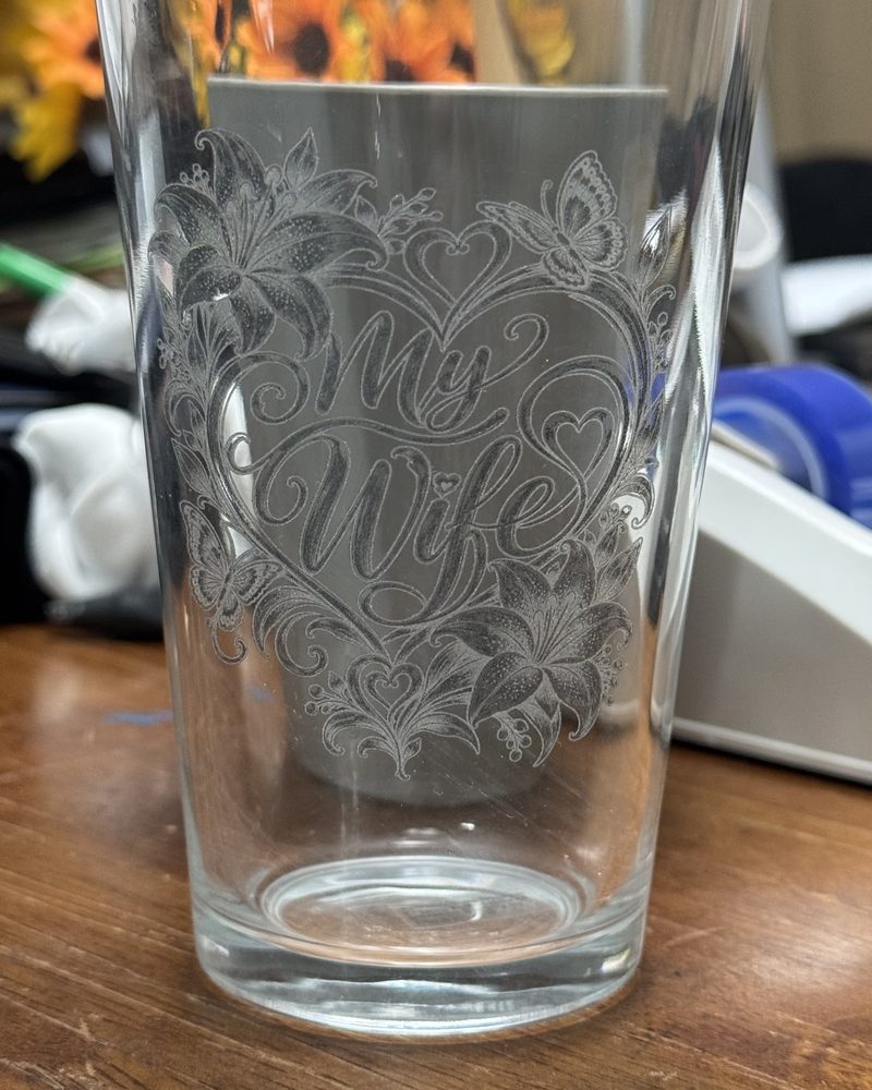 Clear pint glass laser-engraved with "My Wife" in script inside a heart framed by lilies, butterflies and small hearts